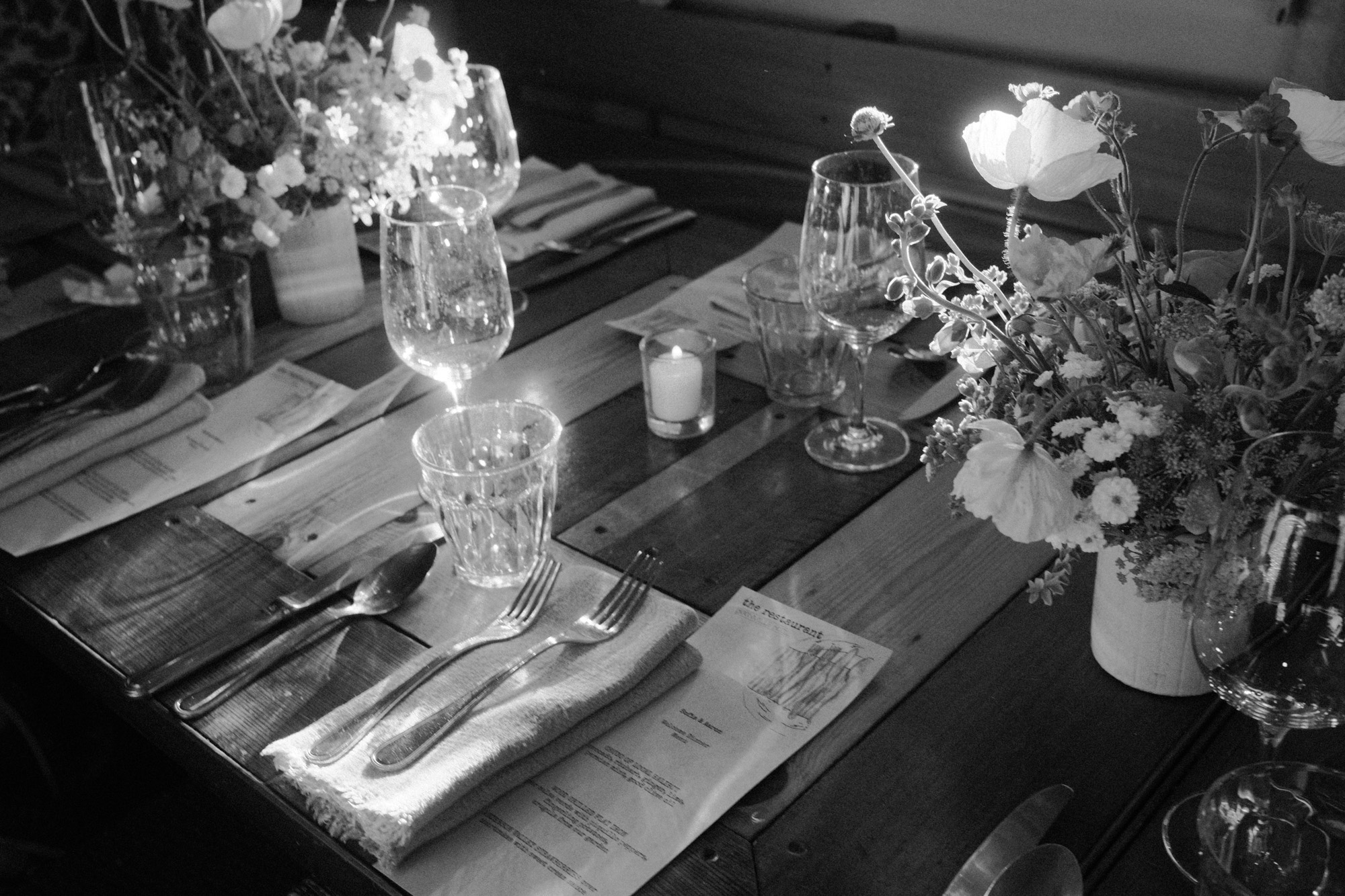 Black-and-white documentary photograph of a wedding table with flowers, glasses and place settings.