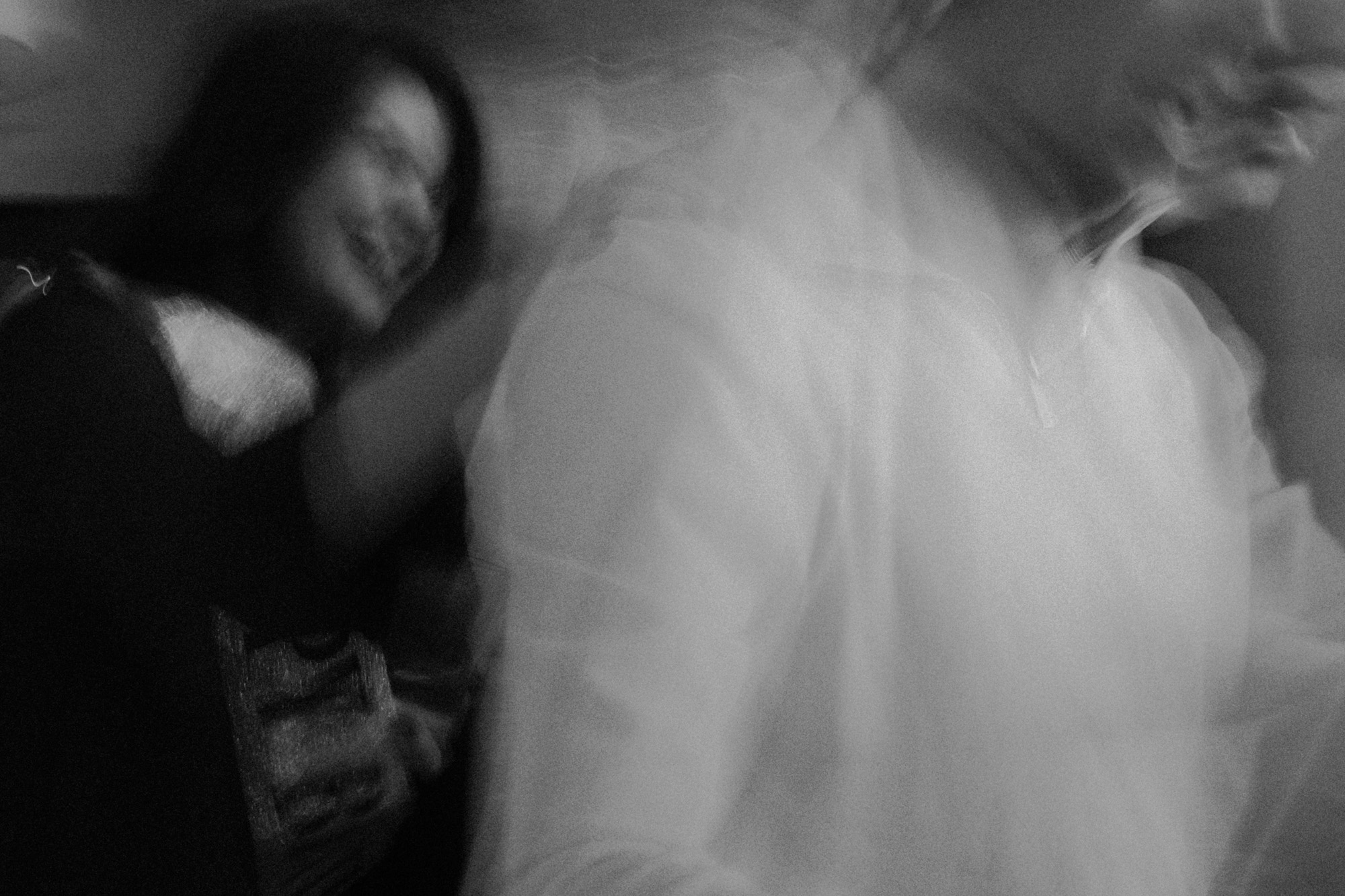 Black-and-white documentary photograph of a blurred wedding veil and intimate movement.